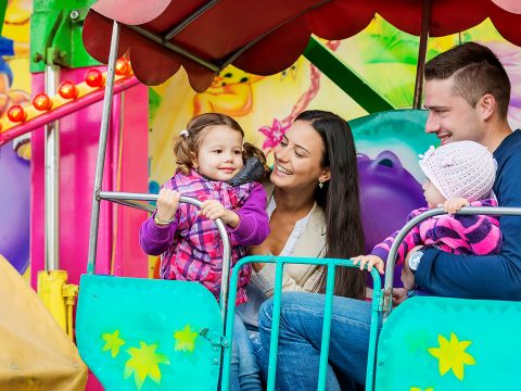 Father, mother, daughters enjoying fun fair ride, amusement park; Courtesy of Halfpoint/Shutterstock