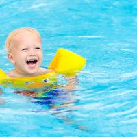 Toddler swimming in pool with swim floaties on; Courtesy of FamVeld/Shutterstock.com