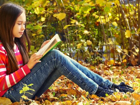 Girl reading outdoors in park.