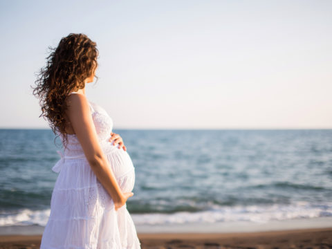 Pregnant woman in white dress standing on the beach