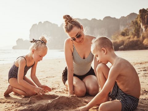 Mom In One Piece Bathing Suit with Kids on Beach; Courtesy of Flamingo Images/Shutterstock.com