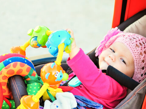 happy baby in the stroller playing toys; Courtesy of Elena Stepanova/Shutterstock