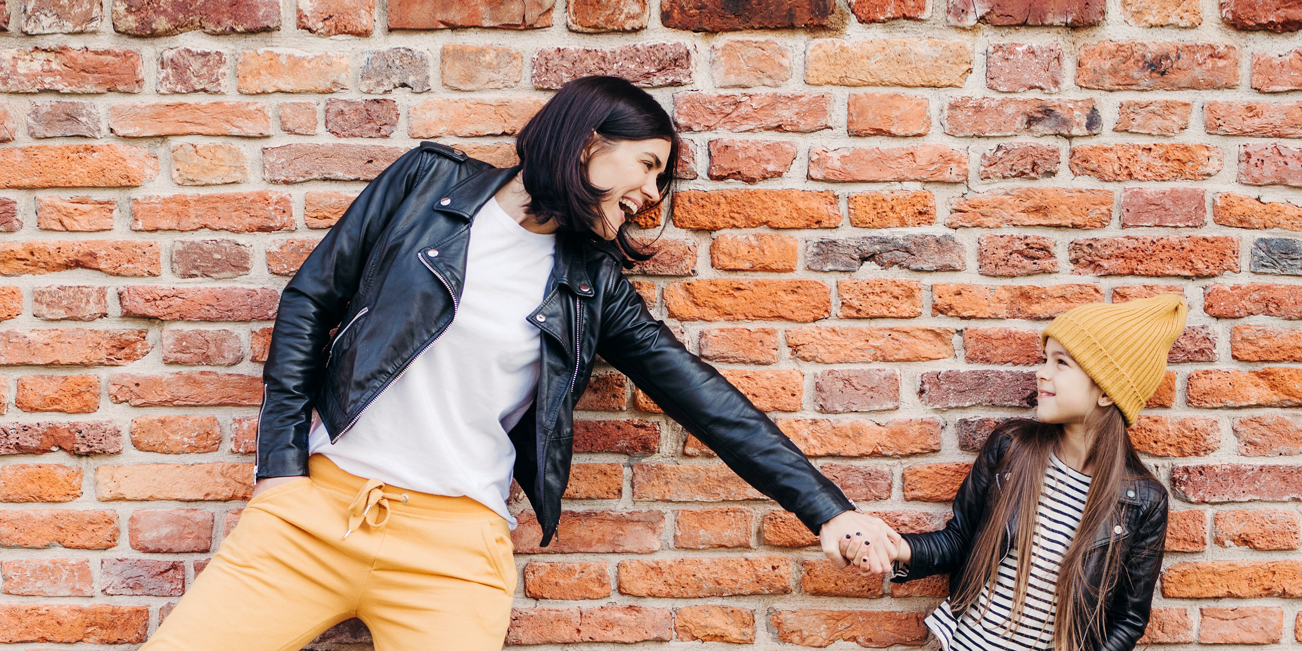 girl and her mother have fun together, keep hands together, pose against brick wall. ; Courtesy of VK Studio/Shutterstock