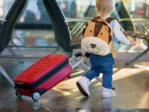 toddler wheeling luggage at airport.; Courtesy of Tomsickova Tatyana/Shutterstock