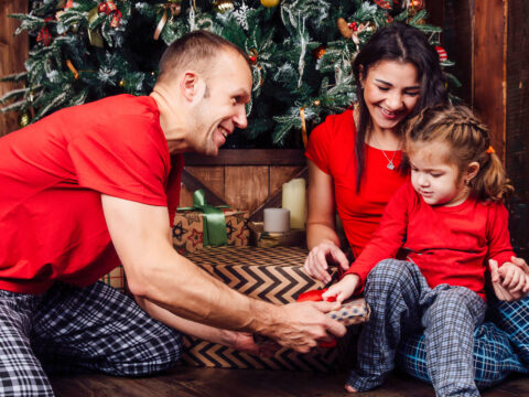 family in pajamas plays next to a Christmas tree and a fireplace. ; Courtesy of vhpicstock /Shutterstock
