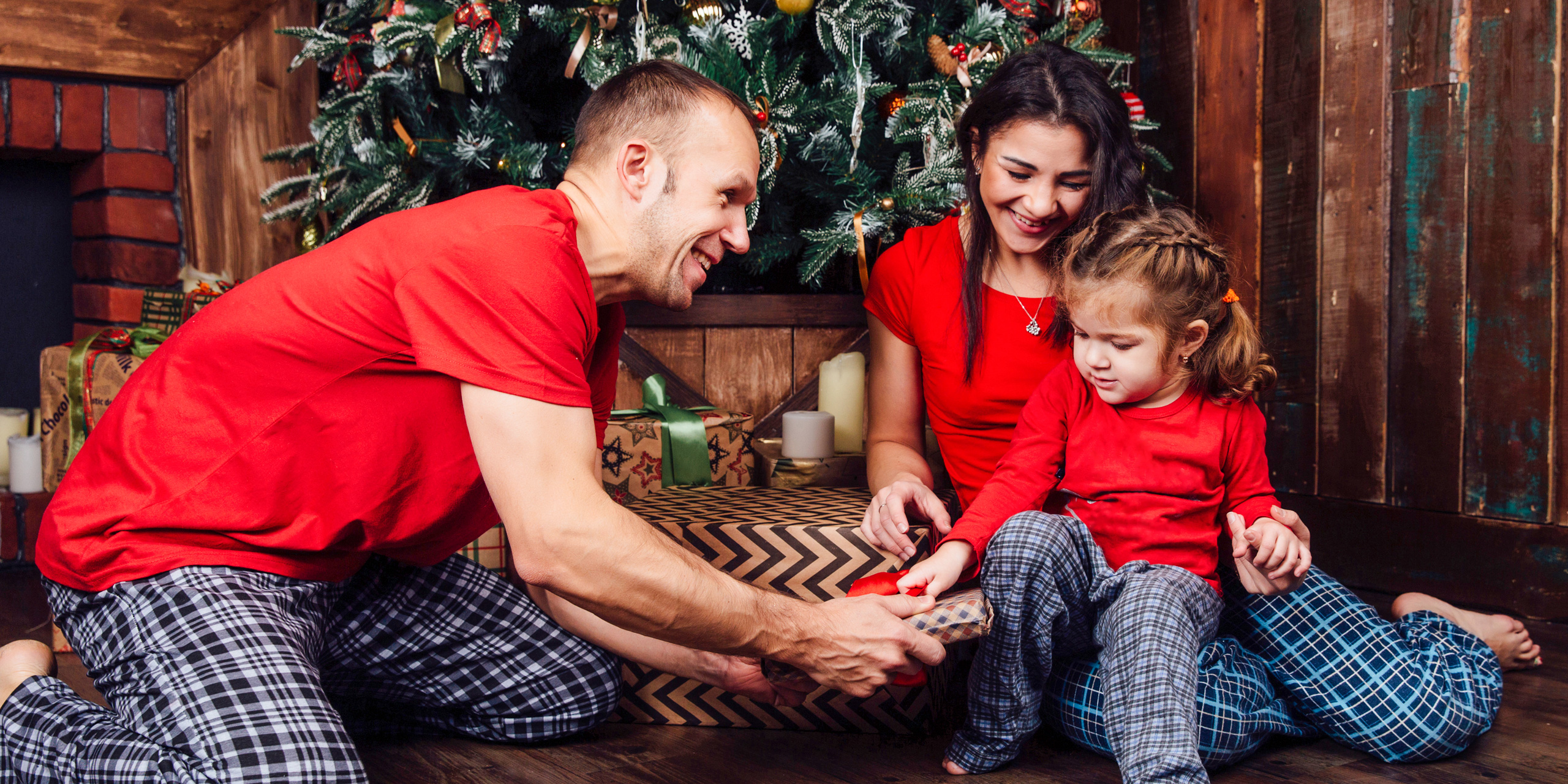 family in pajamas plays next to a Christmas tree and a fireplace. ; Courtesy of vhpicstock /Shutterstock