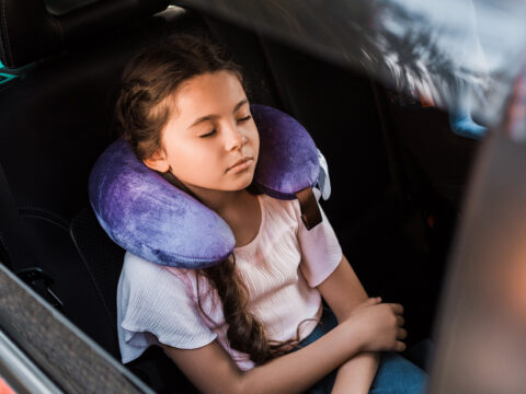 kid sleeping in car with neck pillow; Courtesy of LightField Studios/Shutterstock