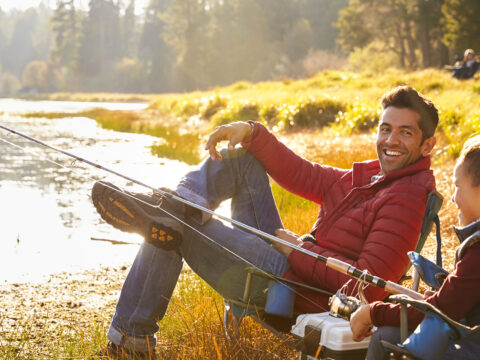 dad sitting with son camping by lake wearing jacket; Courtesy Monkey Business Images/Shutterstock