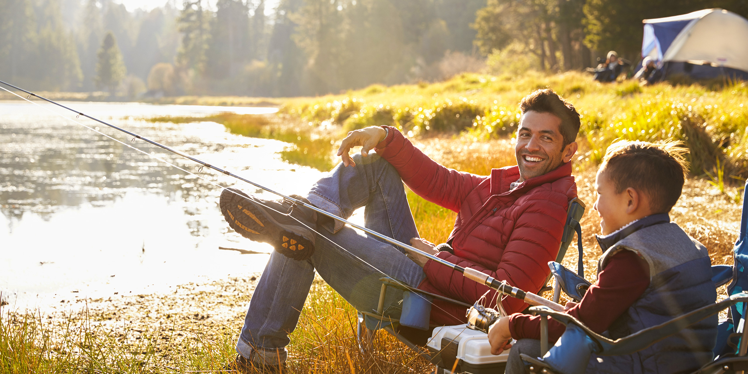 dad sitting with son camping by lake wearing jacket; Courtesy Monkey Business Images/Shutterstock