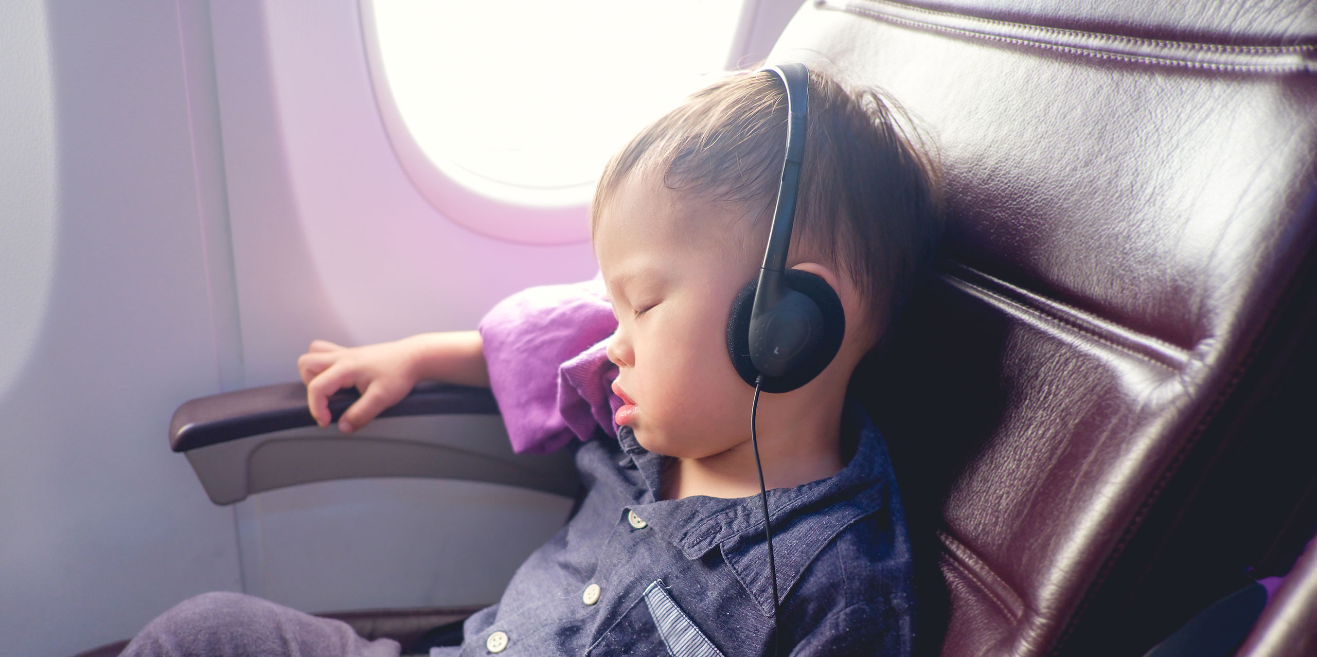 Asian Toddler Wearing Headphones on Plane; Courtesy of Yaoinlove/Shutterstock.com