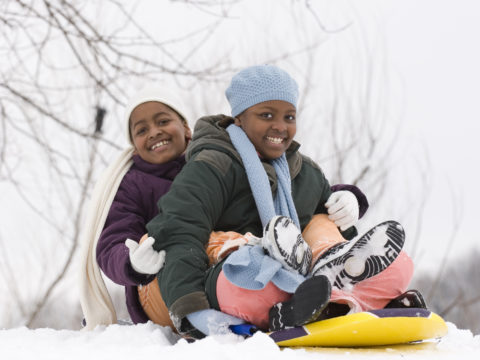 Two children smiling on a sled in the snow