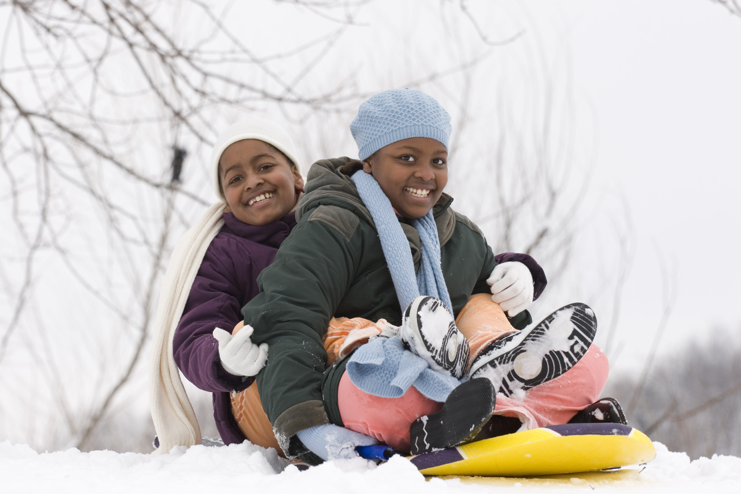 Two children smiling on a sled in the snow