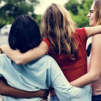 Four young women laugh and walk with their arms around each other