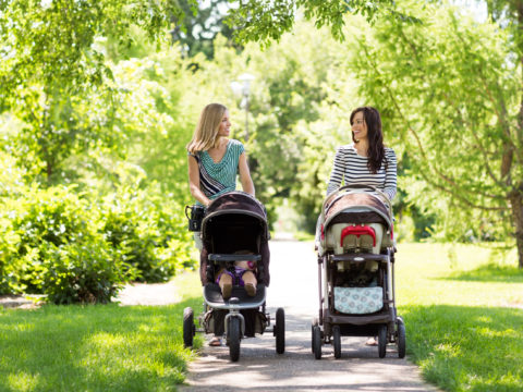 Two women pushing two babies in two strollers in the park