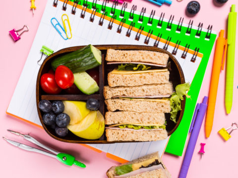 Flat-lay of fully packed school lunch box on top of notebooks and school supplies