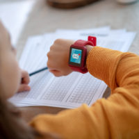 Girl doing homework and looking at her smartwatch, which shows an alert to a new message